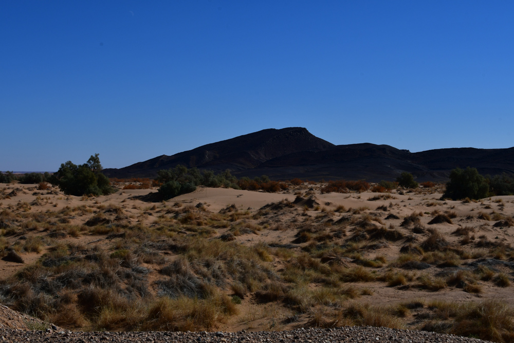 Dunkler Berg vor sandiger Landschaft Bueschel